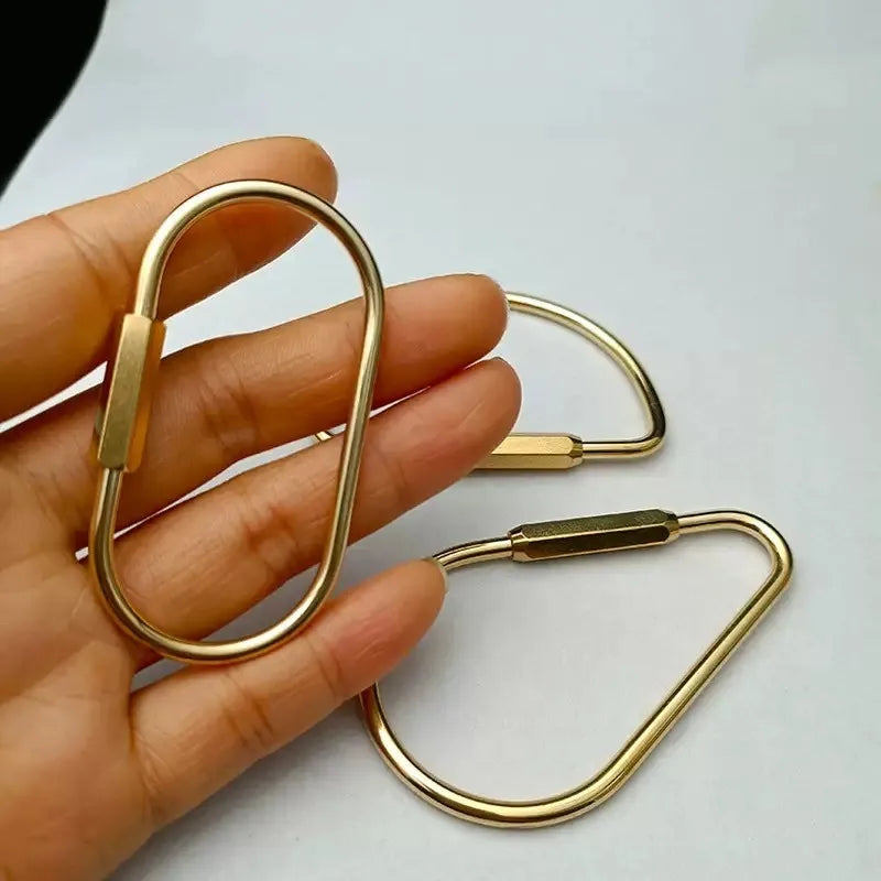 A hand holds a gold brass keychain charm with a locking carabiner clip.