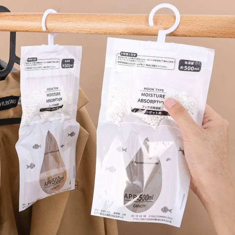 A hand hangs a white moisture absorber bag labeled APP 500ml on a wooden hanger.