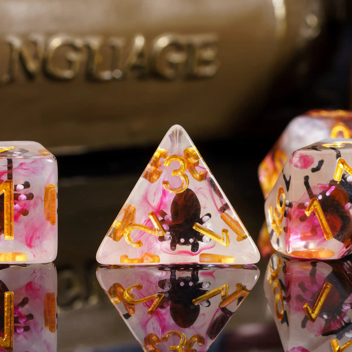 A close-up of pink and gold resin dice set, including a triangular die and its reflection.