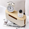 A light wood cable management box with a white alarm clock on top and a glass perfume bottle resting beside it.