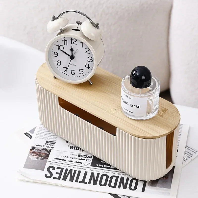 A light wood cable management box with a white alarm clock on top and a glass perfume bottle resting beside it.