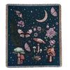 A dark blue woven blanket featuring a botanical and celestial design with moths, roses, mushrooms, and a crescent moon.