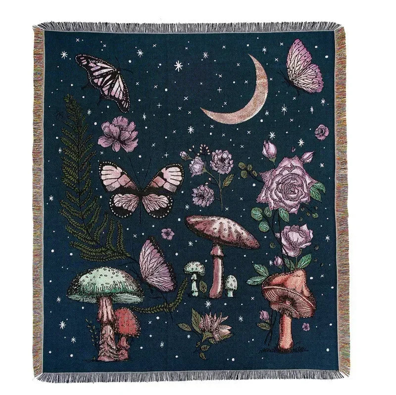 A dark blue woven blanket featuring a botanical and celestial design with moths, roses, mushrooms, and a crescent moon.