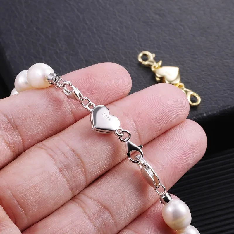 Silver heart-shaped magnetic clasp connecting a pearl bead to a necklace chain.