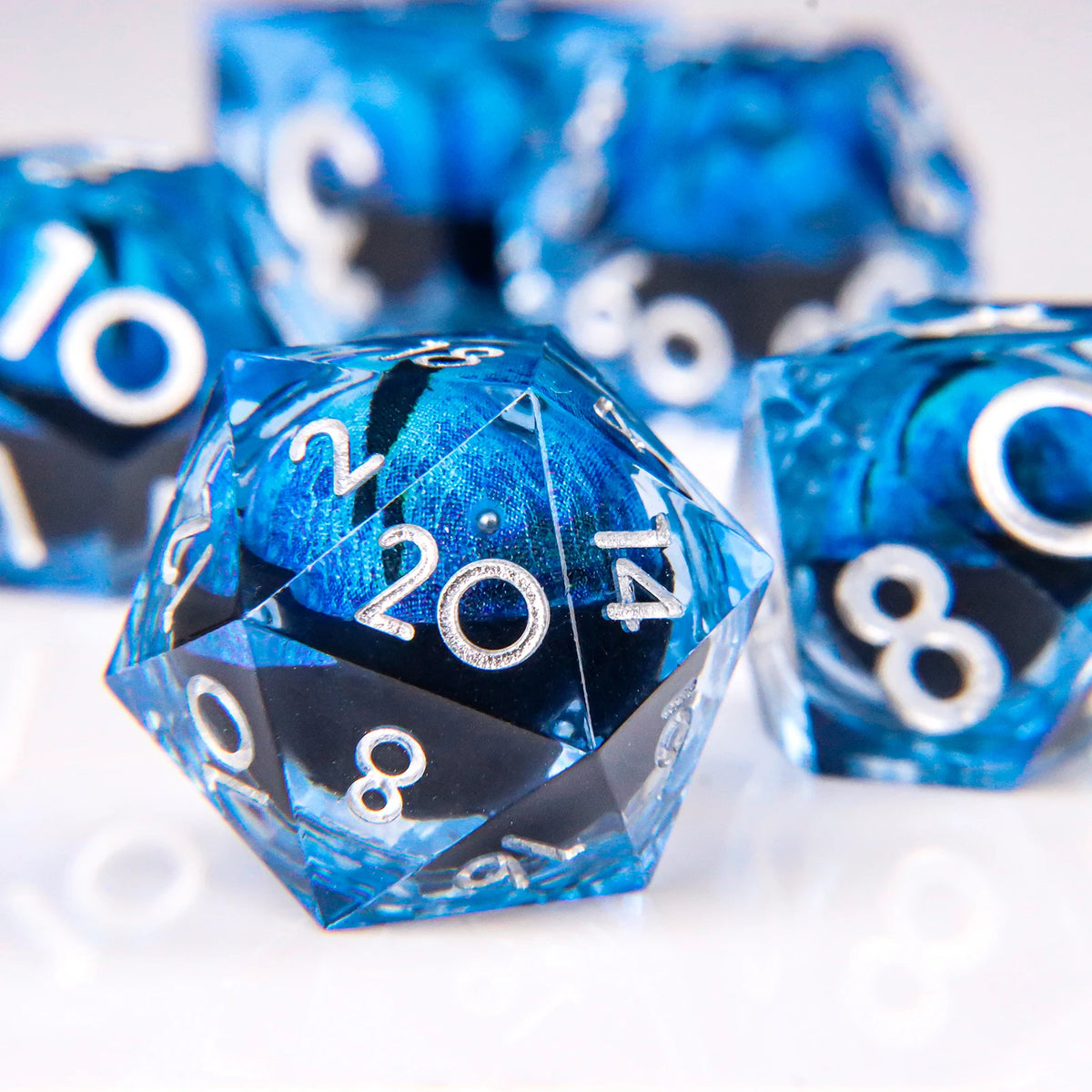 A close-up of a blue liquid core resin die showing the number 20, set against a blurred background of similar dice.