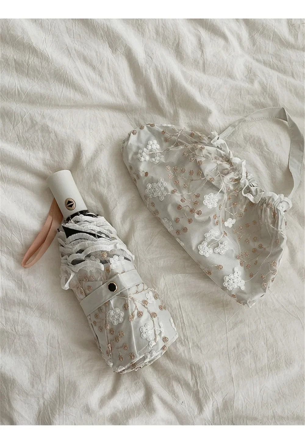 A white lace double-layer folding umbrella with a light pink handle is shown on a white fabric background.