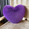 A vibrant purple plush heart-shaped throw pillow resting on a light wooden surface.