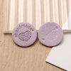 Two round, purple felt labels with a hand-made heart design placed on a light wooden surface.