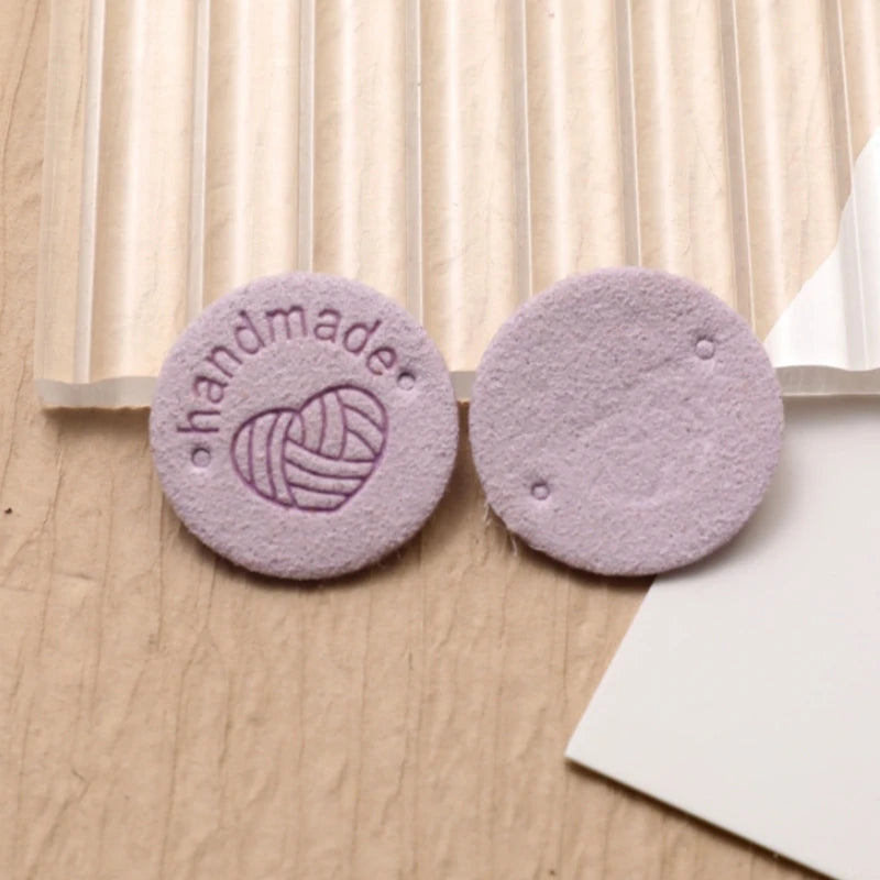 Two round, purple felt labels with a hand-made heart design placed on a light wooden surface.