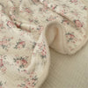 A soft floral muslin baby blanket in cream and pink floral print, folded and draped.