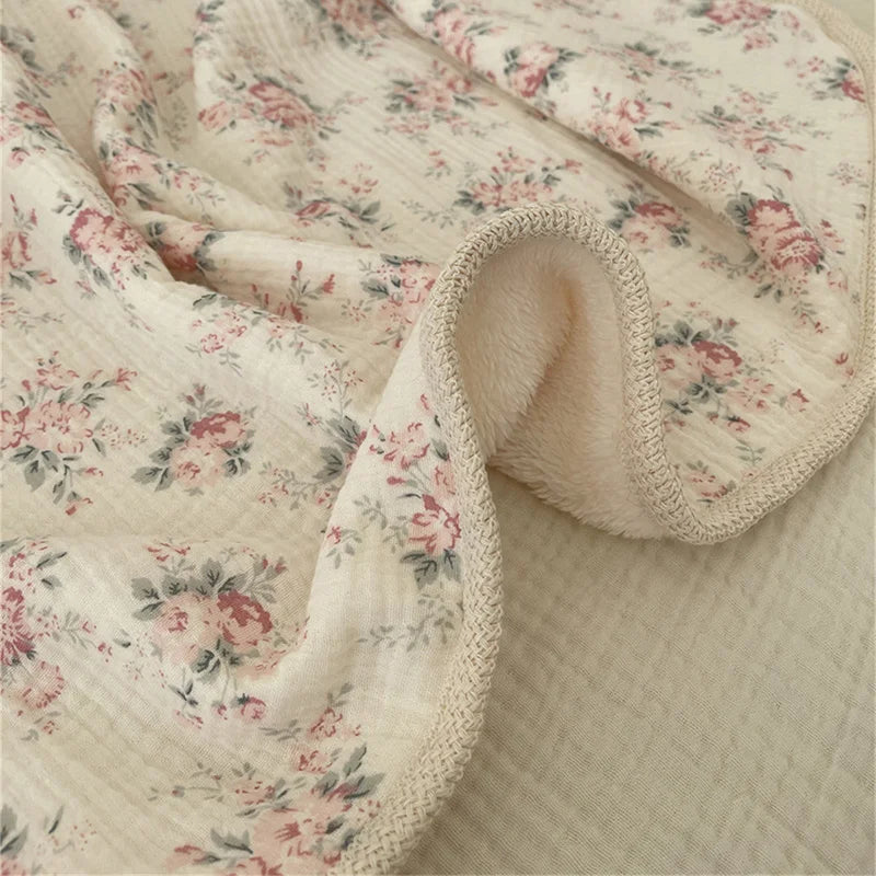 A soft floral muslin baby blanket in cream and pink floral print, folded and draped.
