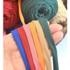 A hand holds several strands of thick polyester blend yarn in various colors including blue, red, pink, orange, beige, and gr