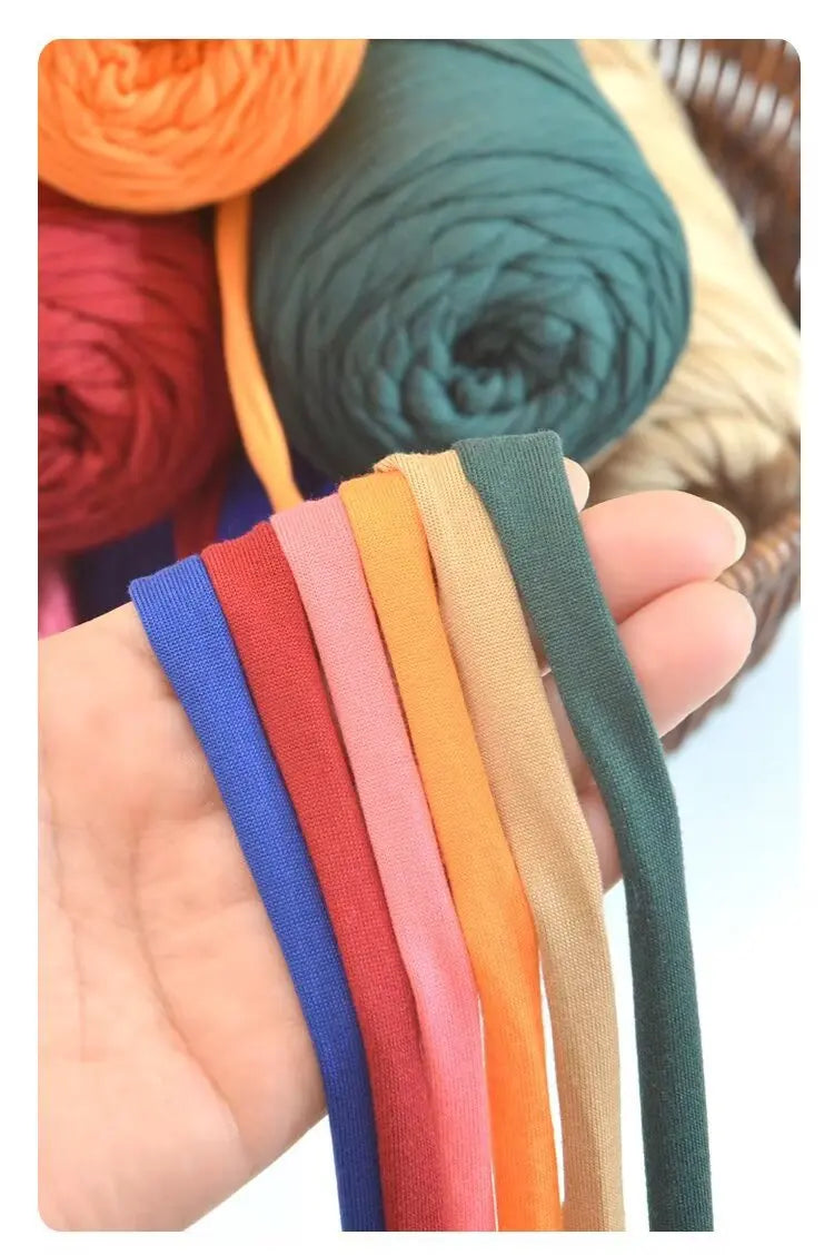 A hand holds several strands of thick polyester blend yarn in various colors including blue, red, pink, orange, beige, and gr