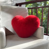 A bright red, fluffy heart-shaped throw pillow resting on a light gray upholstered chair.