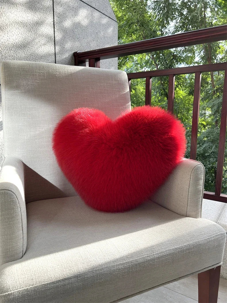 A bright red, fluffy heart-shaped throw pillow resting on a light gray upholstered chair.