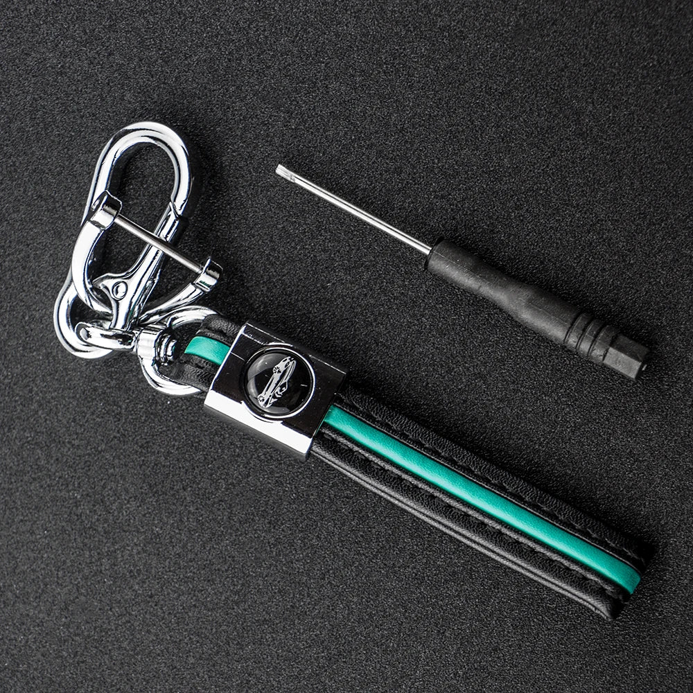 A silver key fob with a protective black TPU cover and a metal tool attached, resting on a dark surface.