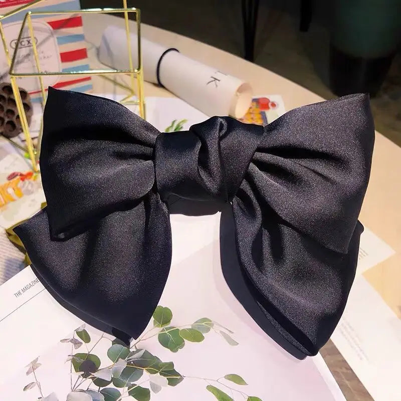 A black silk bow hair clip used as a ponytail holder, displayed on white paper.