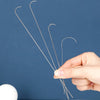 A hand holds three curved stainless steel beading needles against a dark blue background.