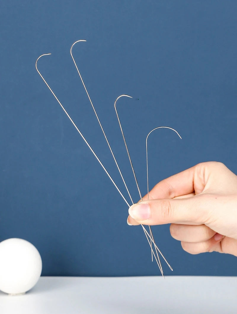 A hand holds three curved stainless steel beading needles against a dark blue background.
