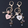 Gold-toned keychain featuring a key and heart charms adorned with clear rhinestones and purple beads.