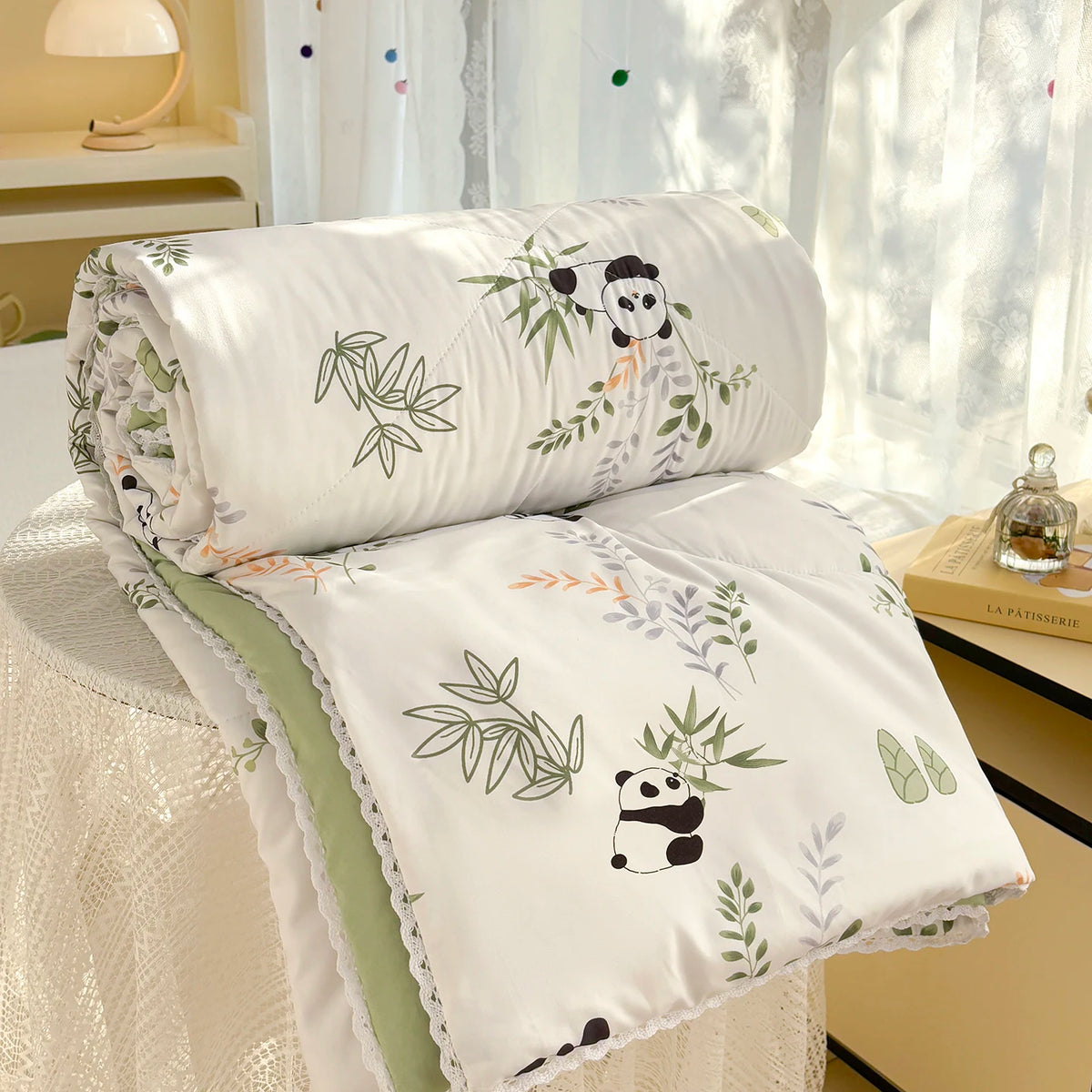 White comforter with a panda print and lace trim resting on a white table.