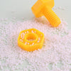 A yellow plastic screw and nut building block resting on a surface covered with small pink and white beads.