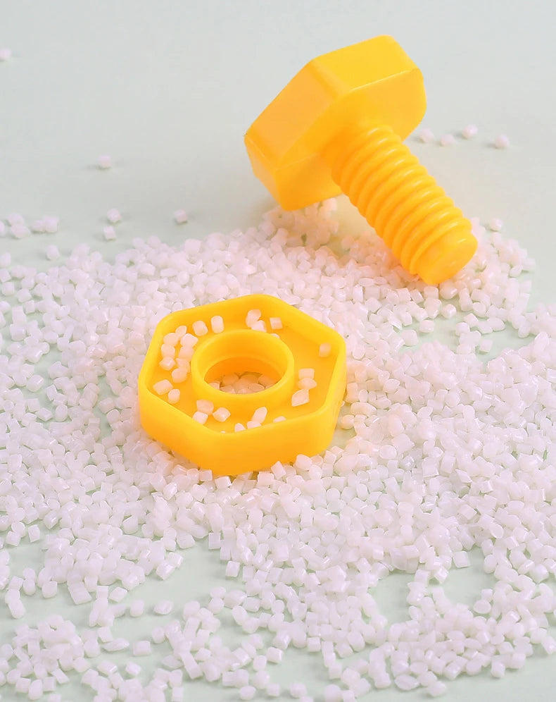 A yellow plastic screw and nut building block resting on a surface covered with small pink and white beads.