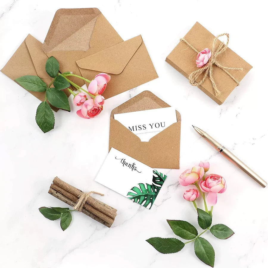 Kraft paper envelopes with pink roses and greenery, including a thank you note.