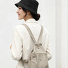 A woman wearing a beige blazer and hat is shown displaying a lightweight mini backpack with an anti-theft chest strap.