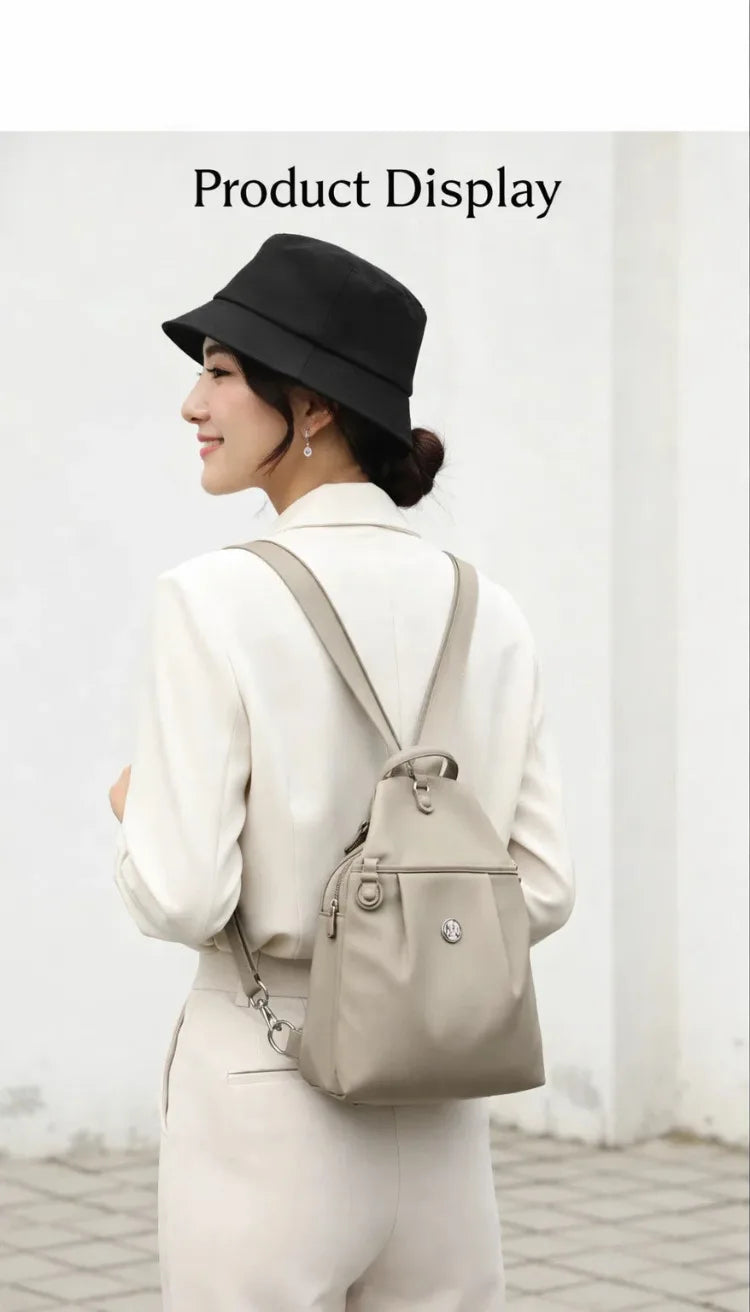 A woman wearing a beige blazer and hat is shown displaying a lightweight mini backpack with an anti-theft chest strap.