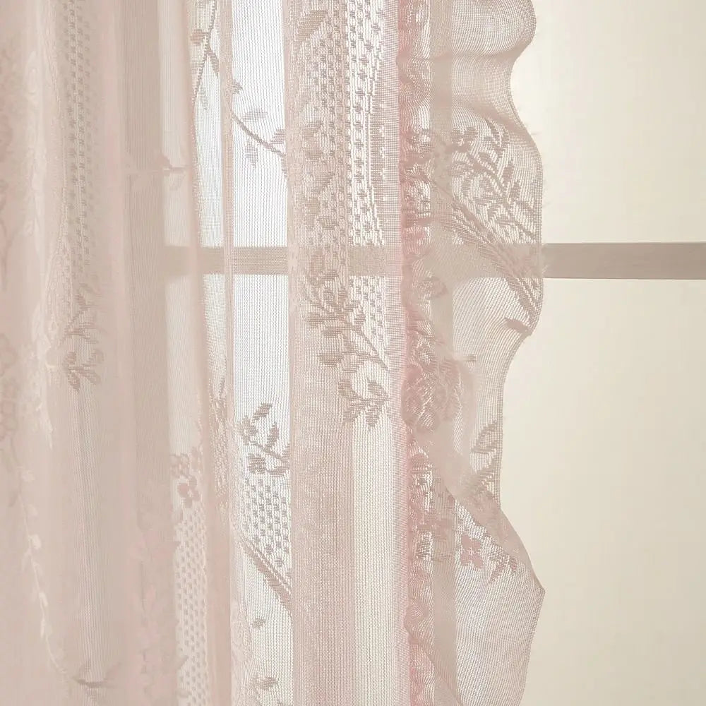 Sheer pink and white ruffled French lace curtains with floral embroidery hanging in a window.