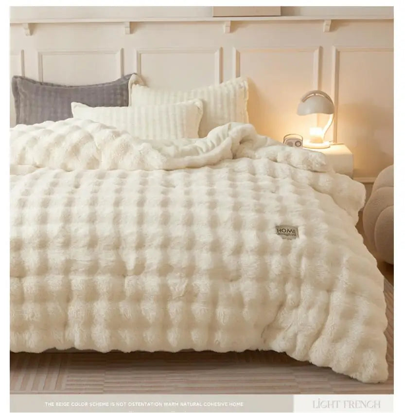 A fluffy white plush winter comforter draped on a bed with light wood and neutral bedding.