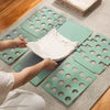 Hands are folding a white t-shirt onto a green plastic board designed for quick and easy clothing organization.