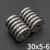 Three countersunk neodymium disc magnets with center holes stacked diagonally on a dark surface.