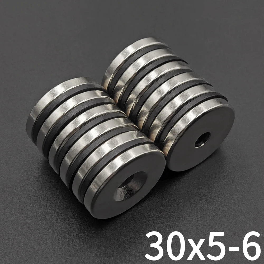 Three countersunk neodymium disc magnets with center holes stacked diagonally on a dark surface.