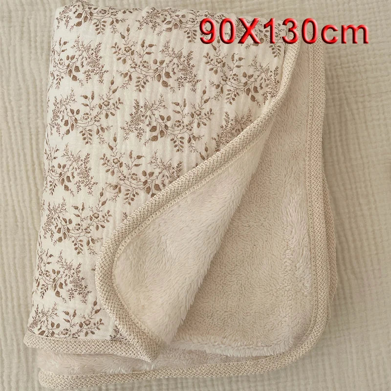 A beige floral muslin baby blanket folded and displayed on a light fabric background.