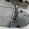 Close-up view of a stainless steel invisible zipper presser foot being inserted into a sewing machine.