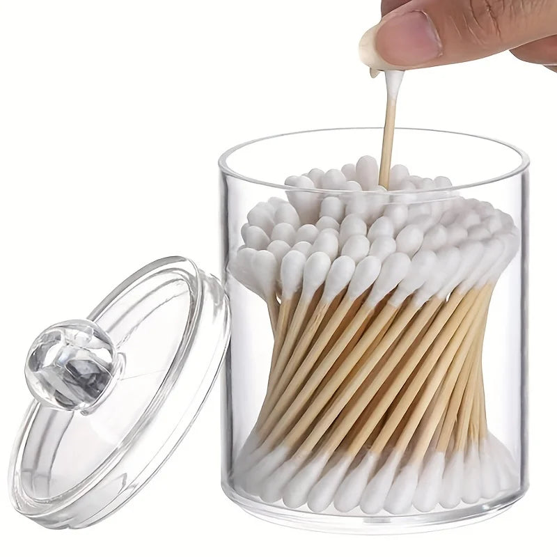Clear acrylic jar holding numerous white cotton balls and swabs for cleaning or cosmetic use