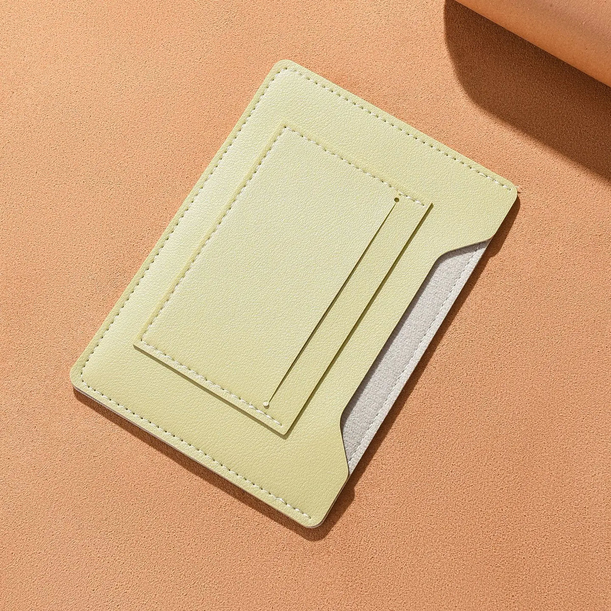 A pale yellow ultra-thin passport holder with a clear plastic window is shown on a beige background.