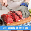 A hand wearing a stainless steel cut-resistant safety glove is holding a piece of fish on a wooden cutting board.