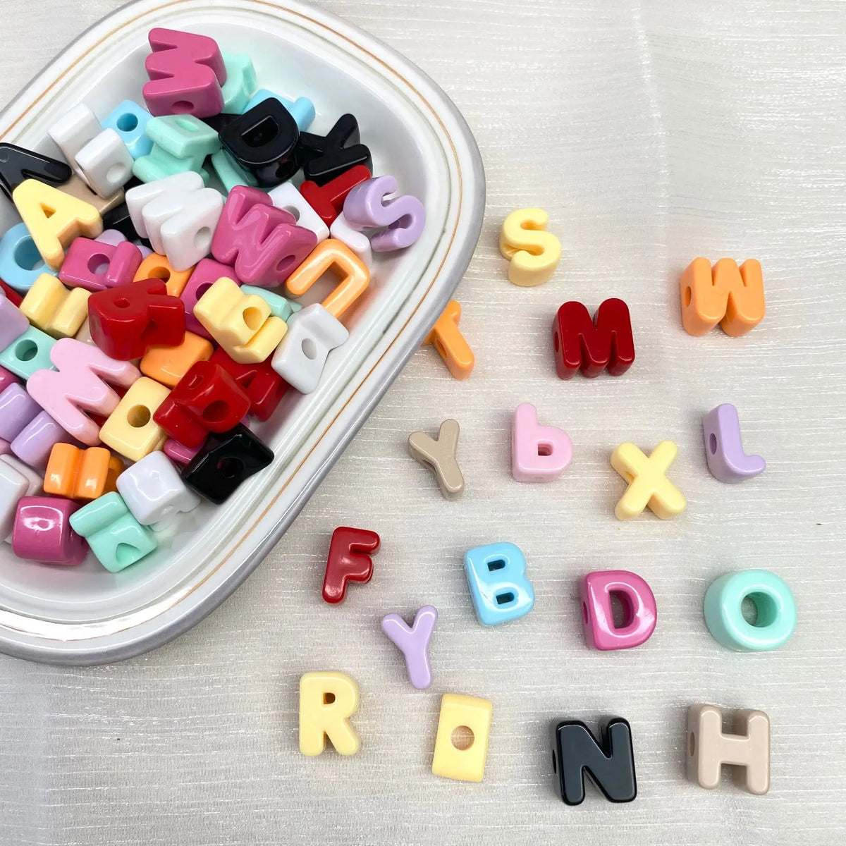 Collection de perles de lettres acryliques colorées de différentes tailles et formes éparpillées sur une surface blanche.