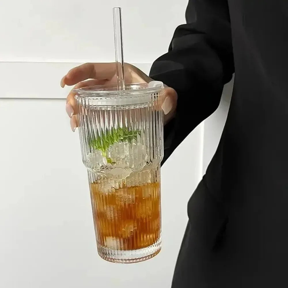 A hand holds a glass tumbler filled with iced tea and mint, featuring a striped glass design.