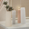 A white silicone mold is shown next to three pillar candles in varying heights on a light wooden surface.