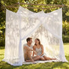 A couple sitting under a sheer white mesh fly net canopy in a grassy outdoor setting.
