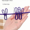 A hand holds a purple elastic travel clothesline with twelve non-slip clips.