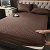 A dark brown quilted mattress protector is shown on a bed, next to a bedside table.