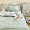 A light mint green quilted bedspread set with embroidered floral patterns and pillows on a bed.