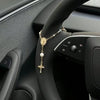 A gold-colored rosary necklace with a cross pendant is displayed on the steering wheel of a car.