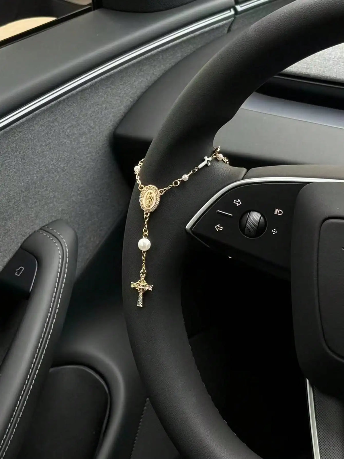 A gold-colored rosary necklace with a cross pendant is displayed on the steering wheel of a car.