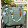 A light green baby bag with a brown strap and a personalized pacifier clip featuring a heart and the name BABY